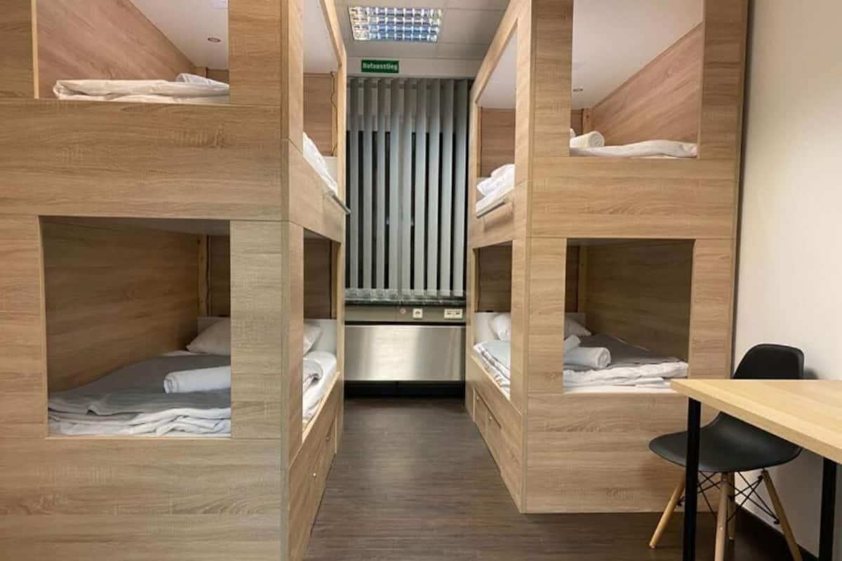 A hotel room with bunk beds, a desk, and a kitchenette.