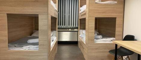 A hotel room with bunk beds, a desk, and a kitchenette.