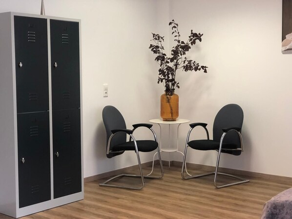 A room with a black metal wardrobe, two black chairs, a small white table, and a potted plant. - Hostel Messe Laatzen (Laatzen)