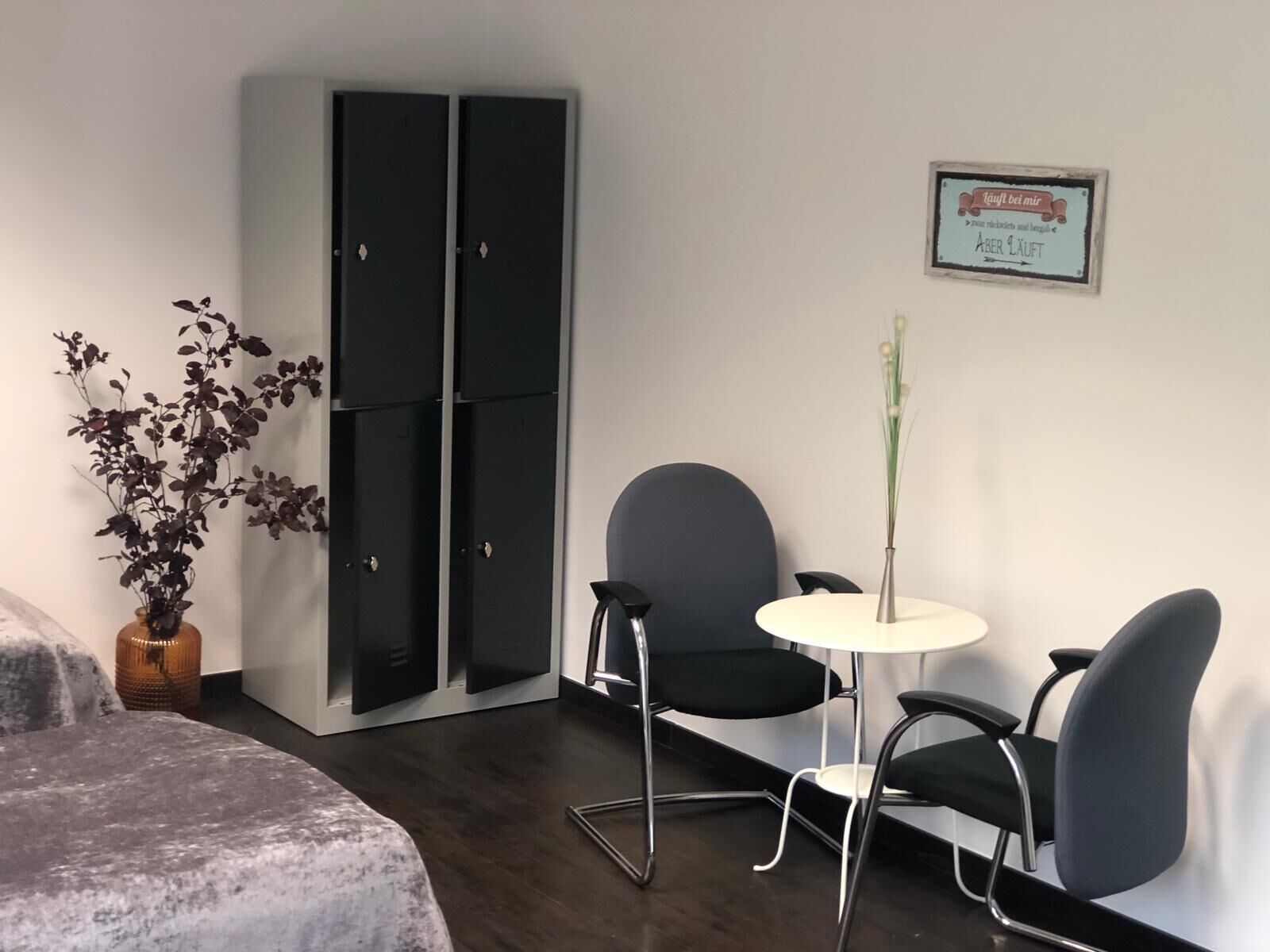 A modern room with a bed, a desk, two chairs, a small table, a potted plant, and a sign on the wall.