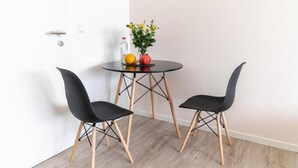 Una habitación pequeña con una mesa redonda, dos sillas negras, un jarrón con flores y una botella.