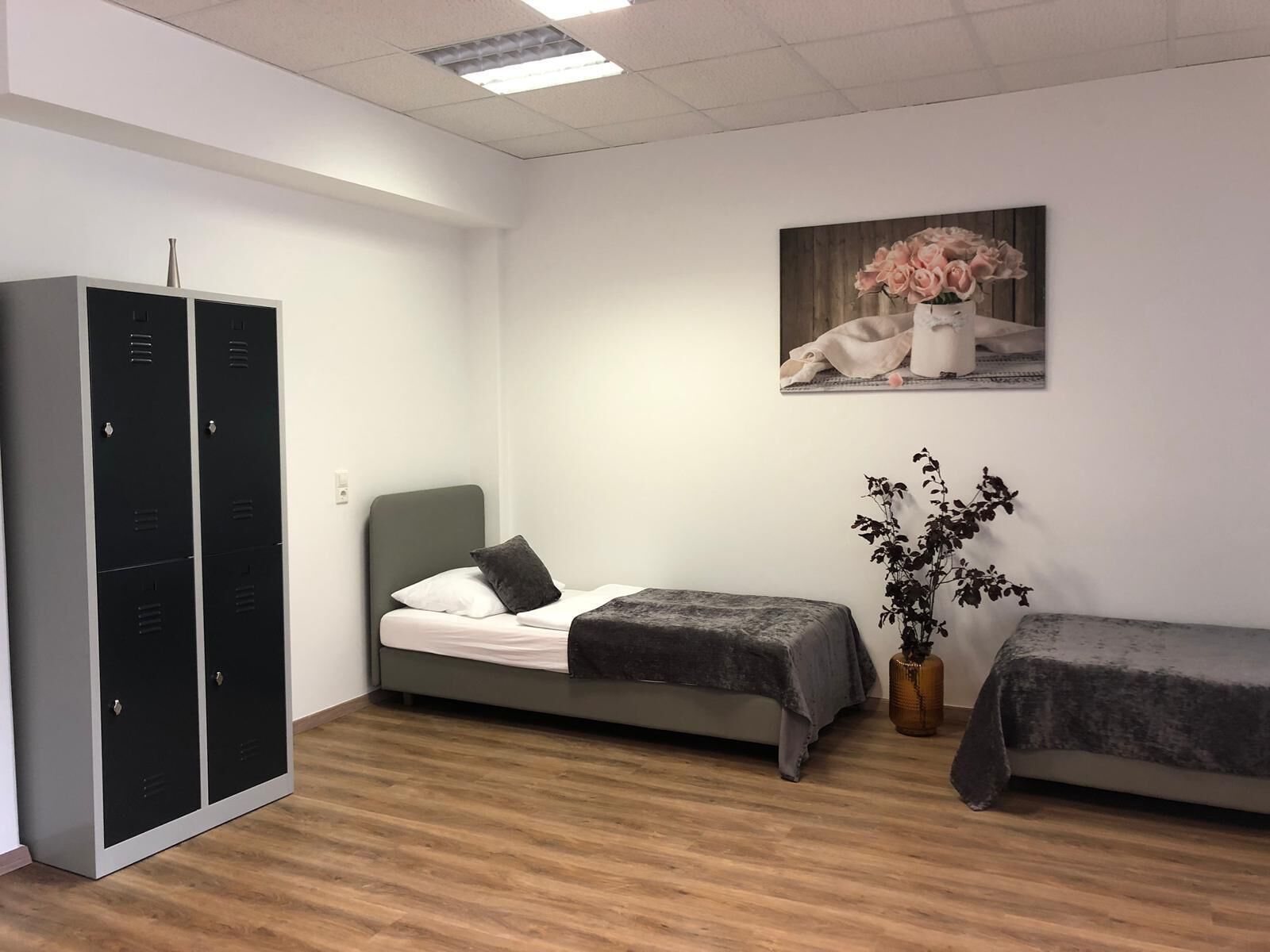 A room with two single beds, a wardrobe, a painting, and a potted plant.
