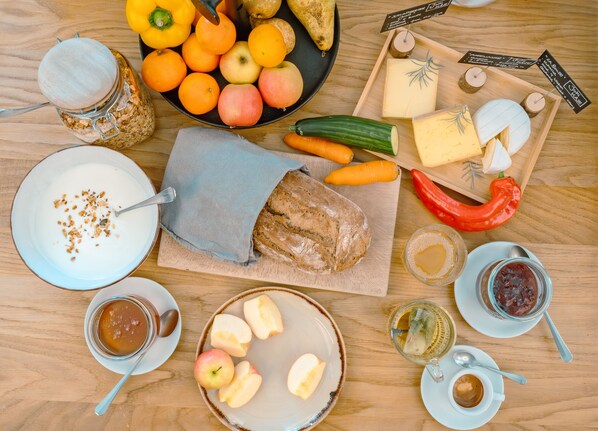 A variety of food items including fruits, vegetables, cheese, bread, and condiments arranged on a wooden table.