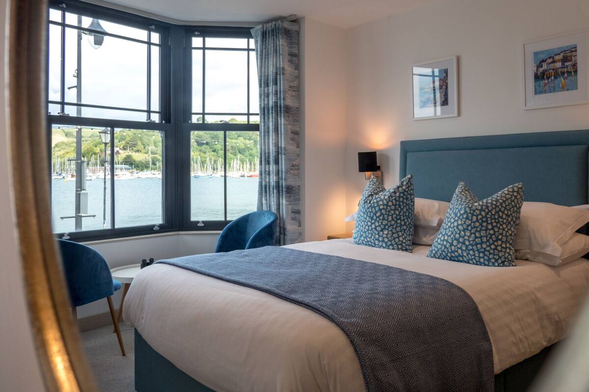Ein Hotelzimmer mit einem großen Bett, Blick auf den Hafen und einem blauen Sessel.