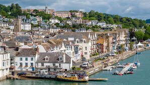 Eine Küstenstadt mit historischen Gebäuden, einem Yachthafen mit Booten und einem markanten Kirchturm.