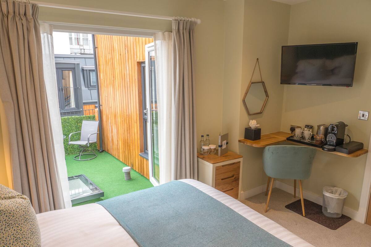 Ein Hotelzimmer mit einem Bett, einem Schreibtisch mit Stuhl, einem Fernseher und einem kleinen Balkon mit Sitzgelegenheit.