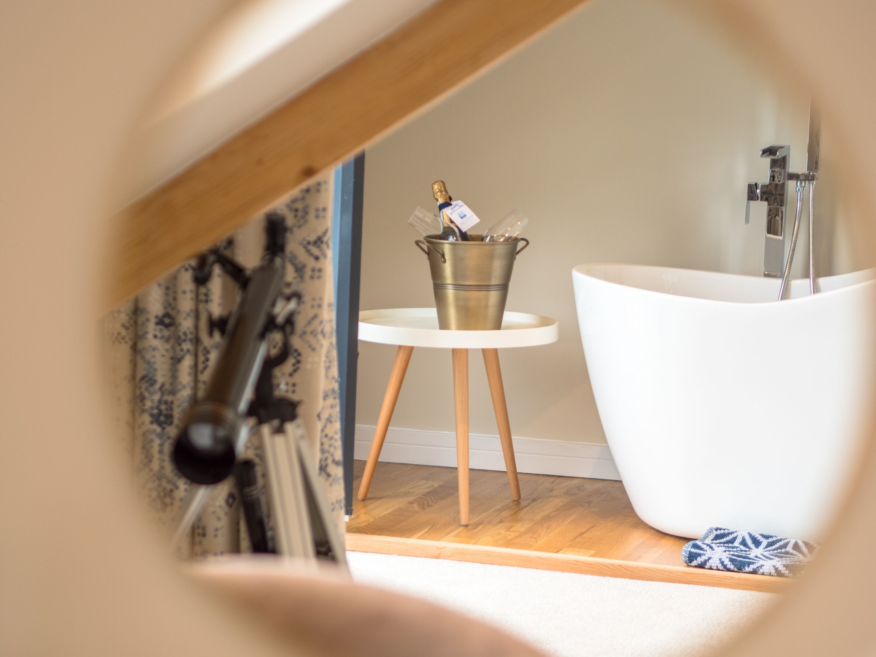 A modern bathroom with a freestanding bathtub, a small round table with a metal bucket, and a towel on the floor.