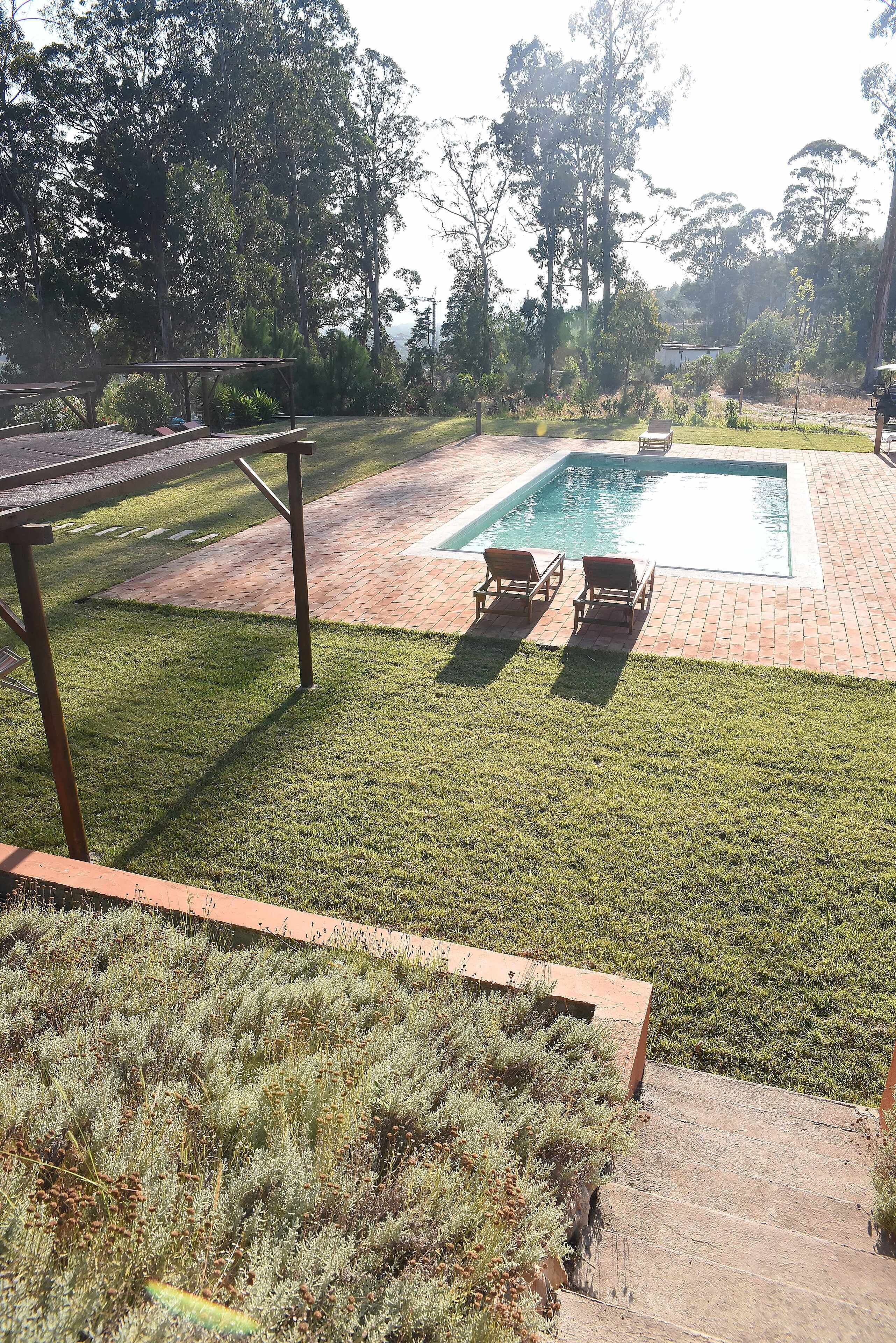 Un patio trasero con piscina, dos sillones de descanso, una pérgola de madera y un césped.
