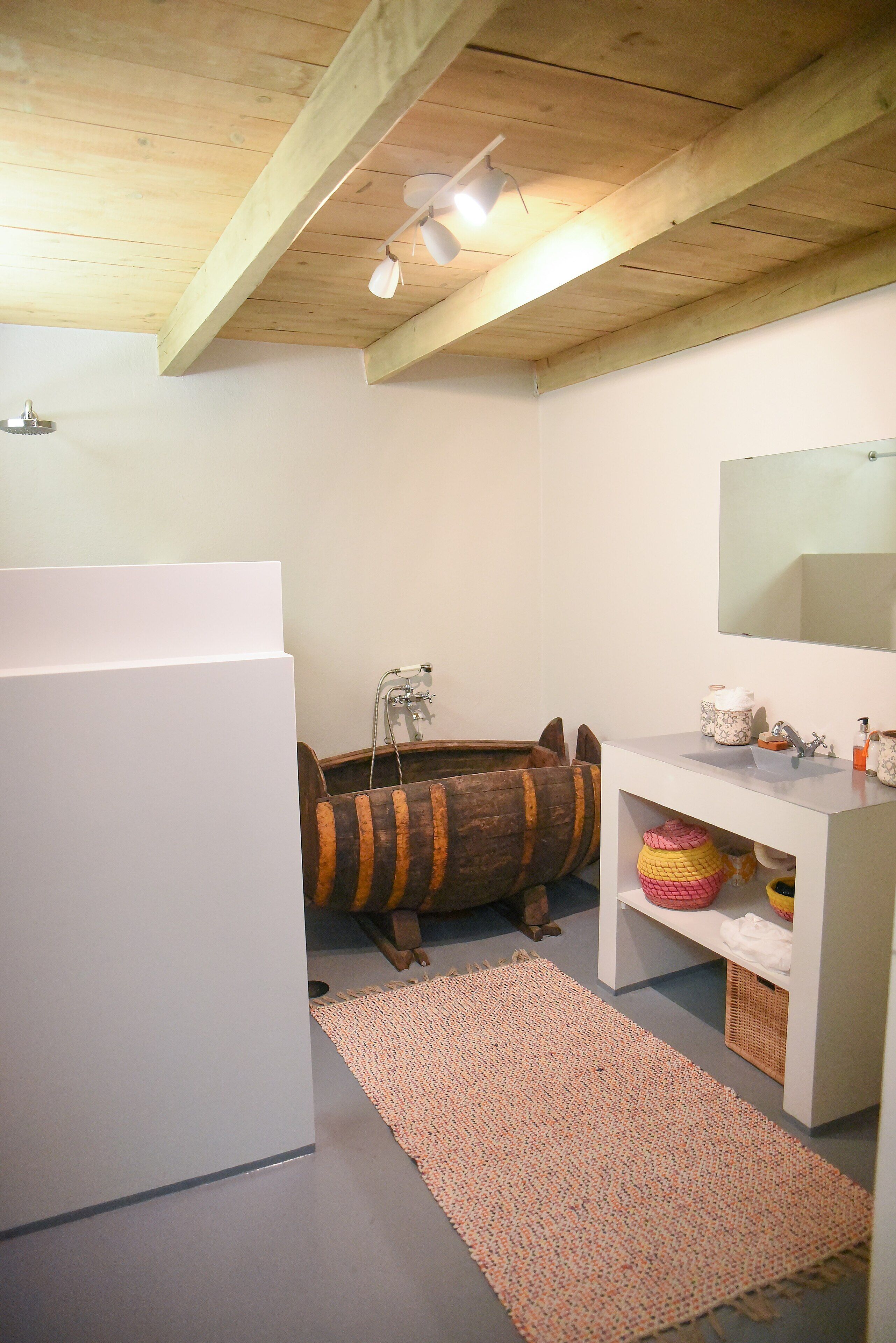 Un baño con techo de madera, un lavabo blanco, un espejo y una pequeña alfombra.