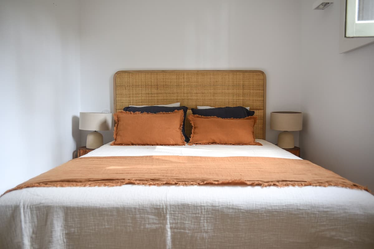 Cama bem arrumada com cabeceira, duas luminárias de cabeceira e um cobertor marrom.