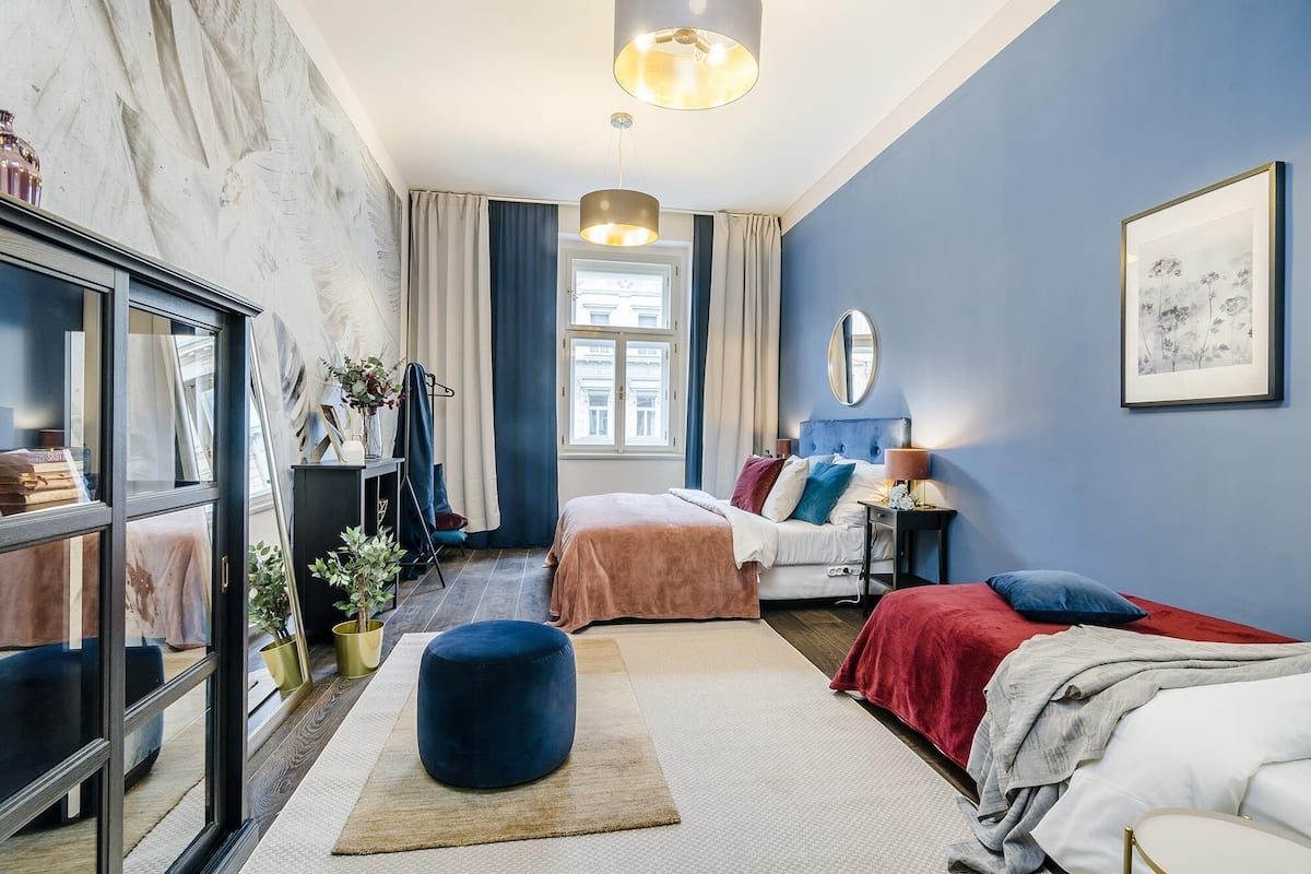Ein modernes Schlafzimmer mit großem Fenster, einem Spiegel und einem Bett mit vielen Kissen.