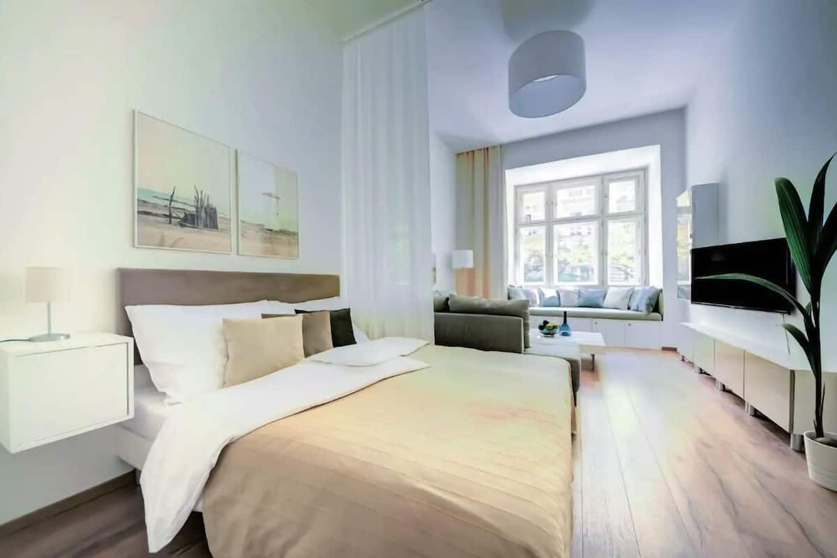 Ein modernes Hotelzimmer mit einem großen Bett, einer Couch, einem Fernseher und einem Fenster mit Vorhängen.