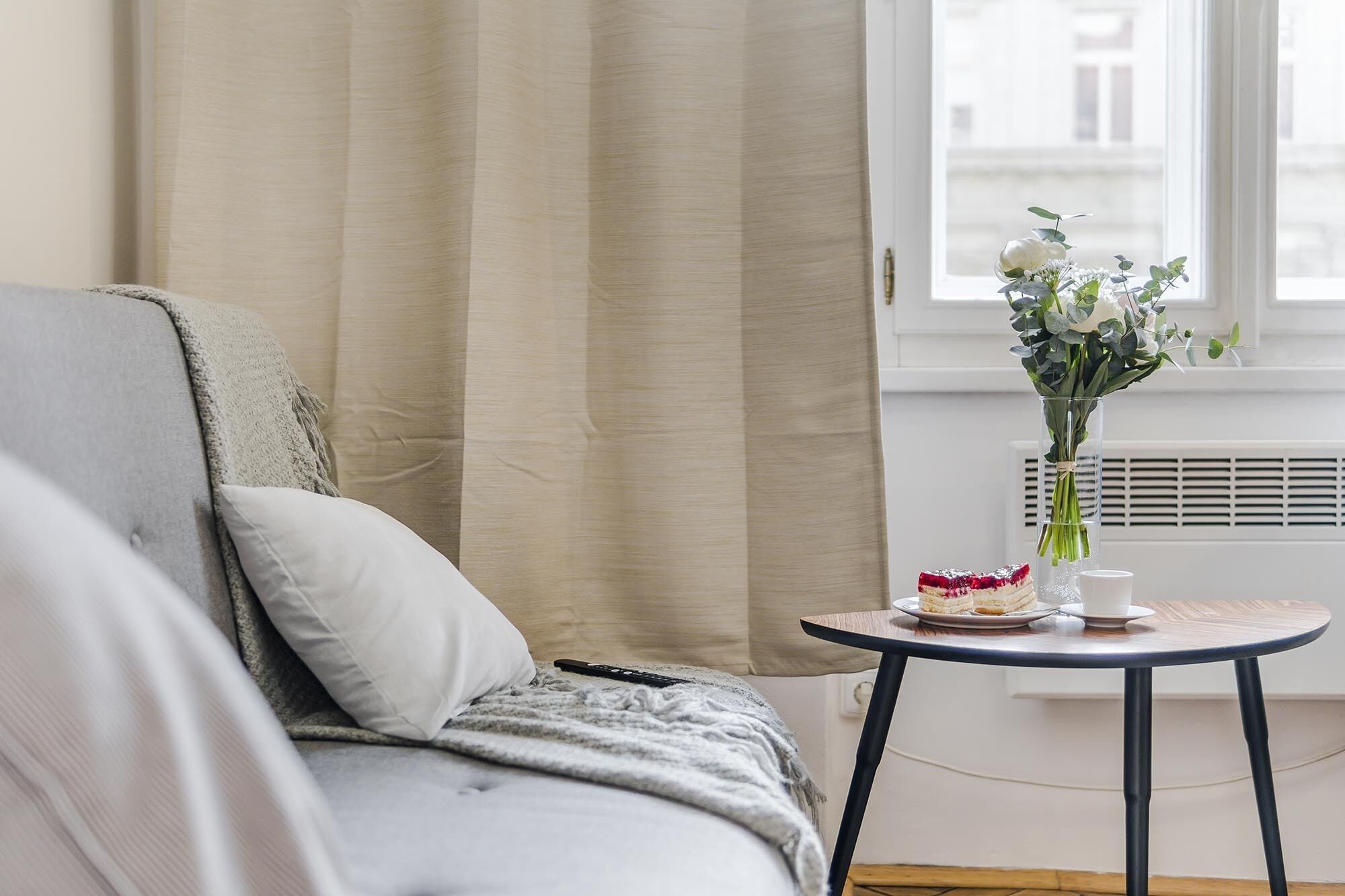 Una habitación acogedora con una cama, una mesita con un florero y una ventana con cortinas.