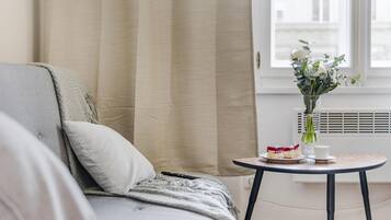 Una habitación acogedora con una cama, una mesita con un florero y una ventana con cortinas.