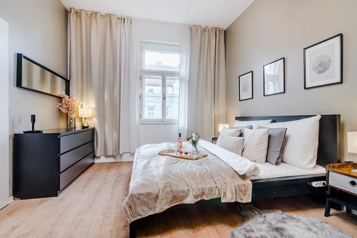 Ein modernes Schlafzimmer mit einem Bett, Nachttischen, einer Kommode und einem Fenster mit Vorhängen.