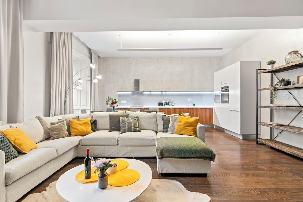Ein modernes Wohnzimmer mit einer Eckcouch, einem Couchtisch und einer Küche im Hintergrund.