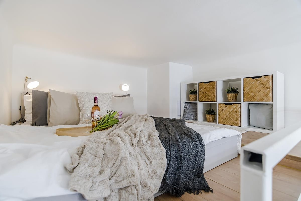 Ein modernes Schlafzimmer mit einem Bett, Nachttischlampen, einer Weinflasche und dekorativen Kissen.