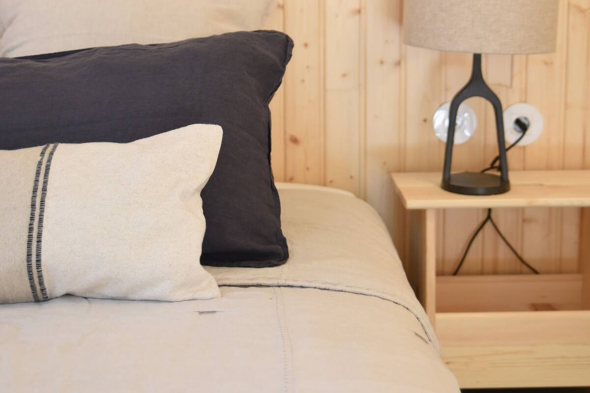 A wooden-paneled room with a bed, pillows, and a bedside table with a lamp.