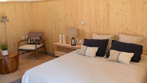 A bedroom with a large bed, a wooden chair, a bedside table, and a small shelf with decorative items. - Vumba - Beira Suite (Arganil)