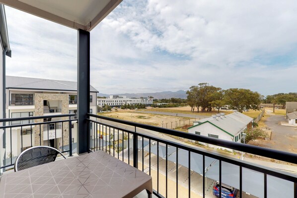 A balcony with a table and chairs, overlooking a residential area with houses and a road.