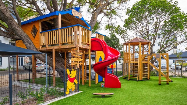 A playground with a red slide, a wooden playhouse, and a Winnie the Pooh statue. - The Jade Estate Somerset West (Cape Town)