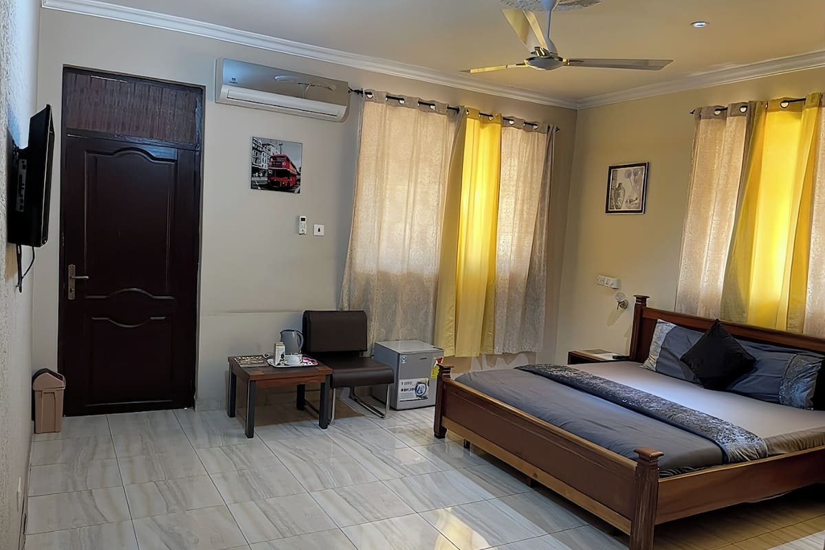 Een hotelkamer met een bed, een bureau, een stoel, een airconditioner en gordijnen.