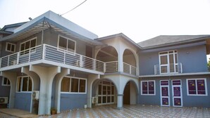 A two-story building with a tiled courtyard, multiple balconies, and a series of doors with signs.