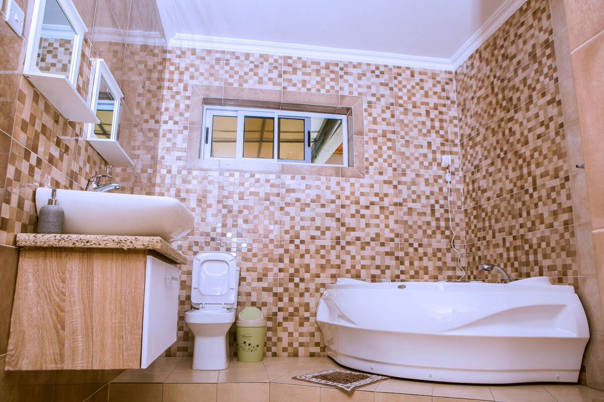 Een badkamer met een betegelde mozaïekwand, een raam, een toilet, een wastafel en een bad.