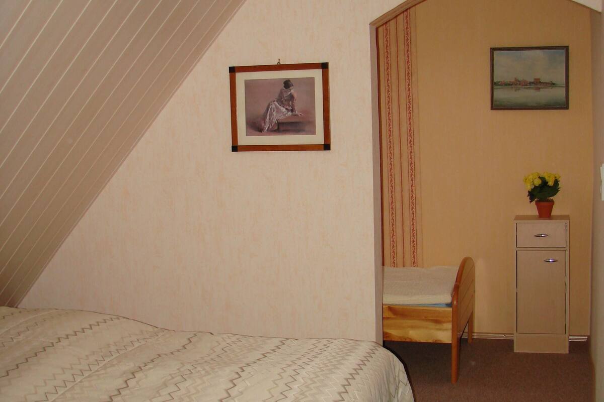 A bedroom with a bed, a desk, a chair, a picture on the wall, and a window with curtains.