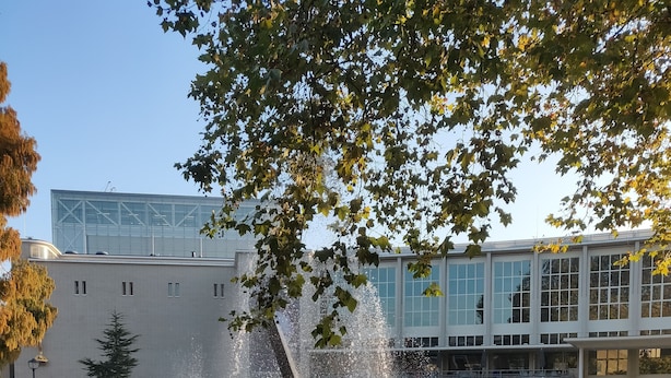 Una fuente con chorros de agua en un parque, con un edificio moderno al fondo.