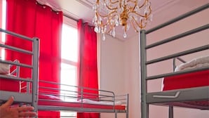 Un dormitorio con literas, cortinas rojas, una araña y suelo de baldosas.
