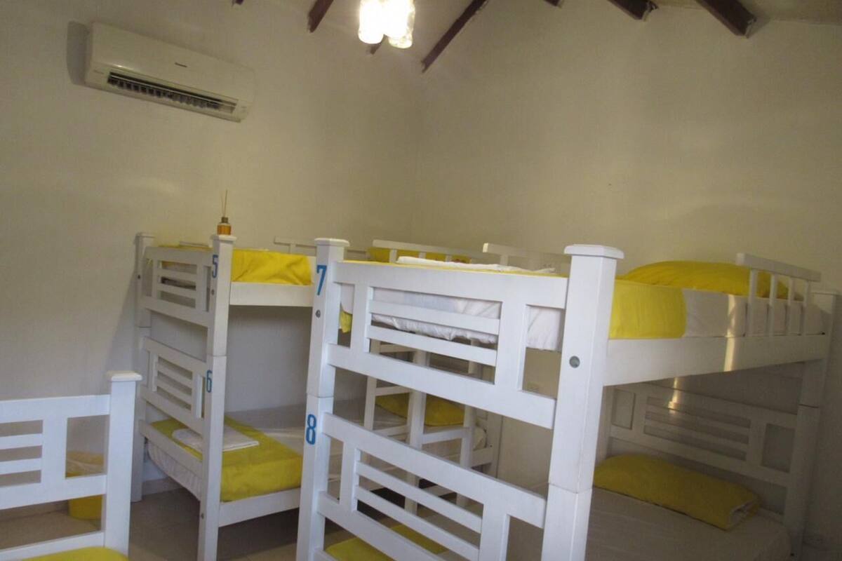 Une chambre avec un lit superposé, dotée de draps blancs et jaunes, d’un climatiseur et d’un plafond en bois.