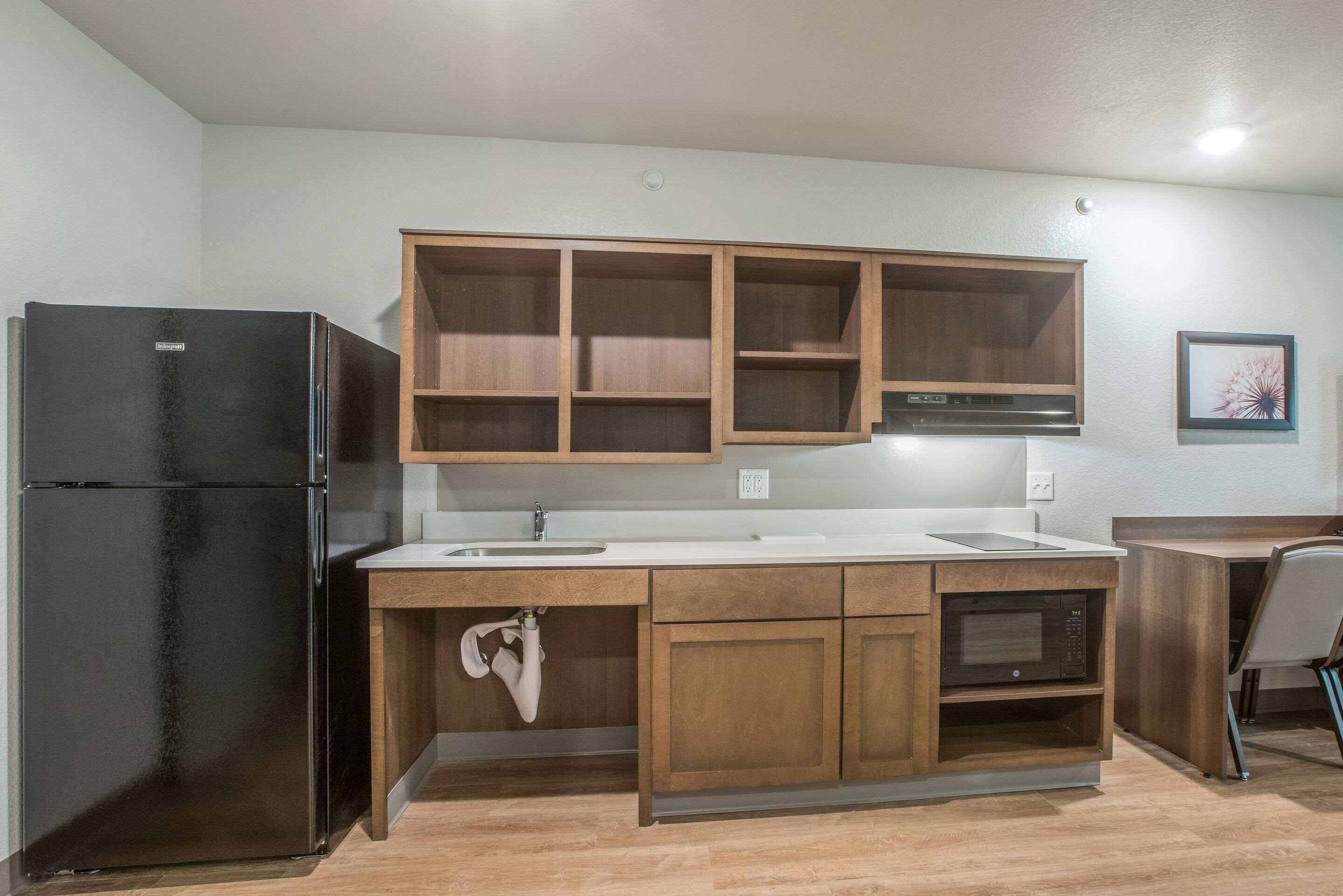 A compact kitchen with a black refrigerator, wooden cabinets, a microwave, and a sink.