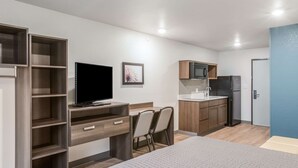 A modern hotel room with a bed, a desk with a flat-screen TV, a kitchenette with a microwave and refrigerator, and a bathroom with a toilet and sink. - WoodSpring Suites Atlanta McDonough (McDonough)