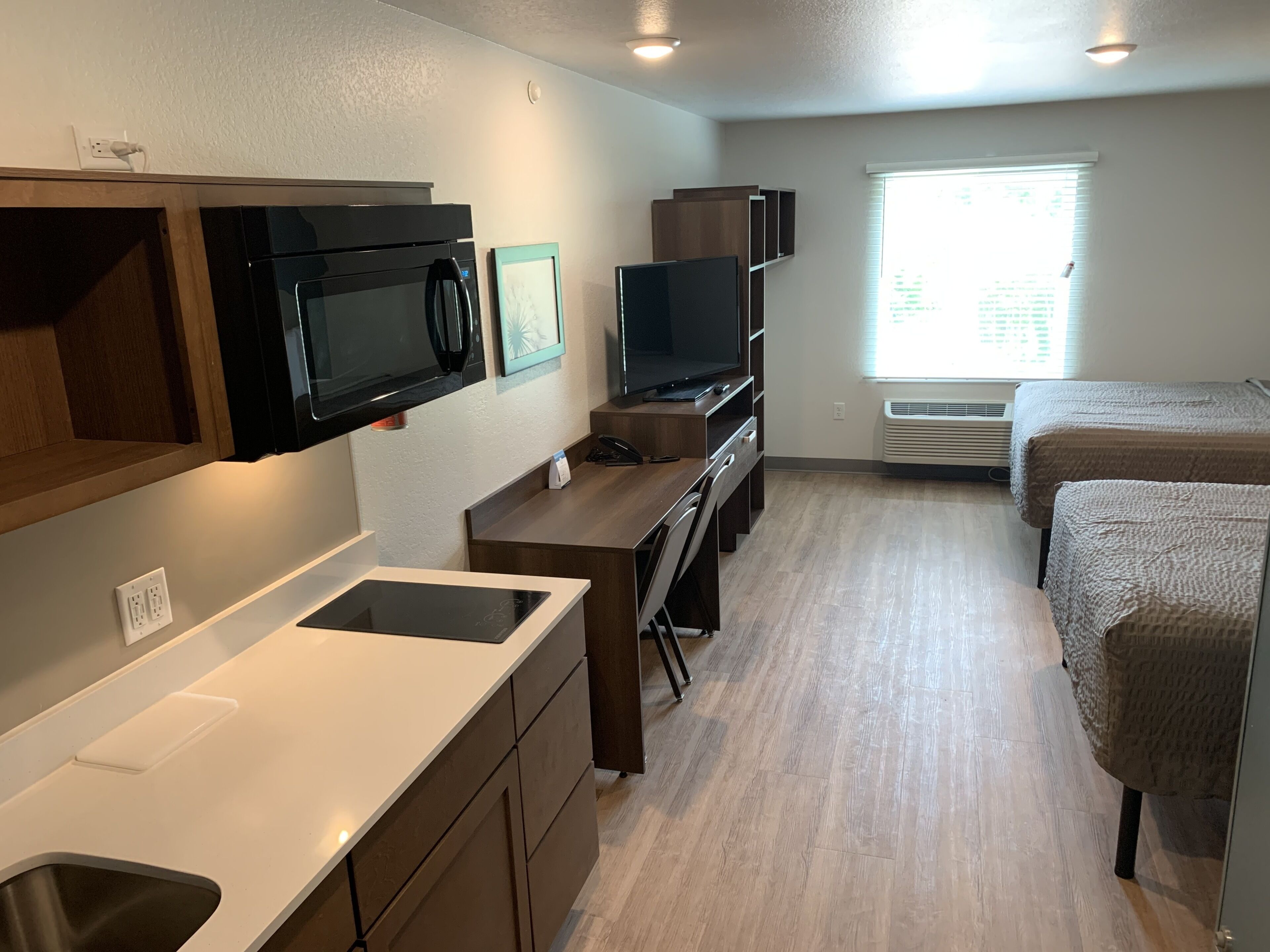 A compact hotel room with a kitchenette, a flat-screen TV, a desk, and a bed.