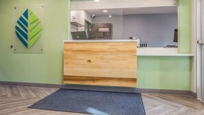 A reception area with a wooden desk, a glass partition, and a green wall. - WoodSpring Suites Atlanta McDonough (McDonough)