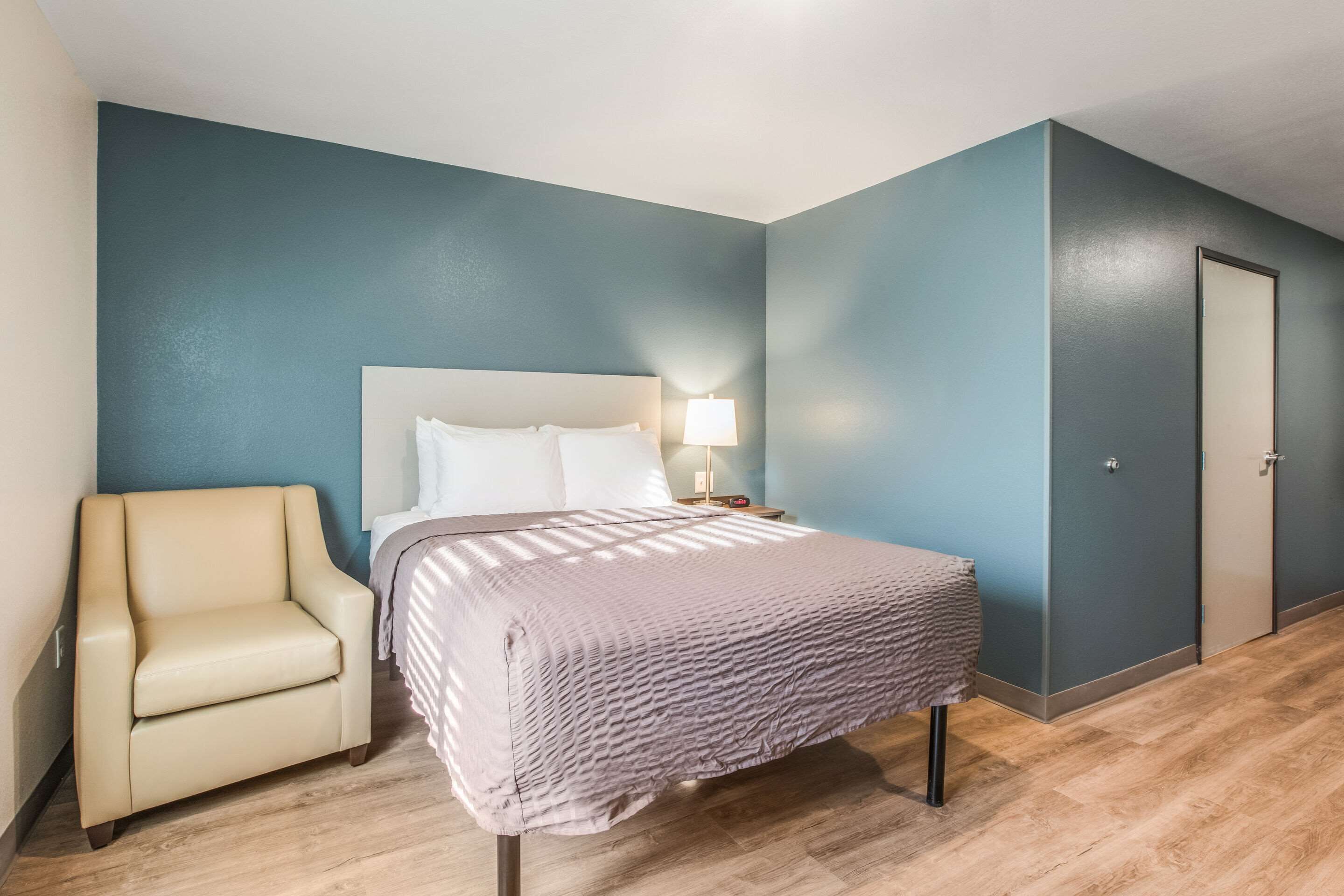 Une chambre à coucher avec un lit, une chaise, une table de chevet avec une lampe et une porte.