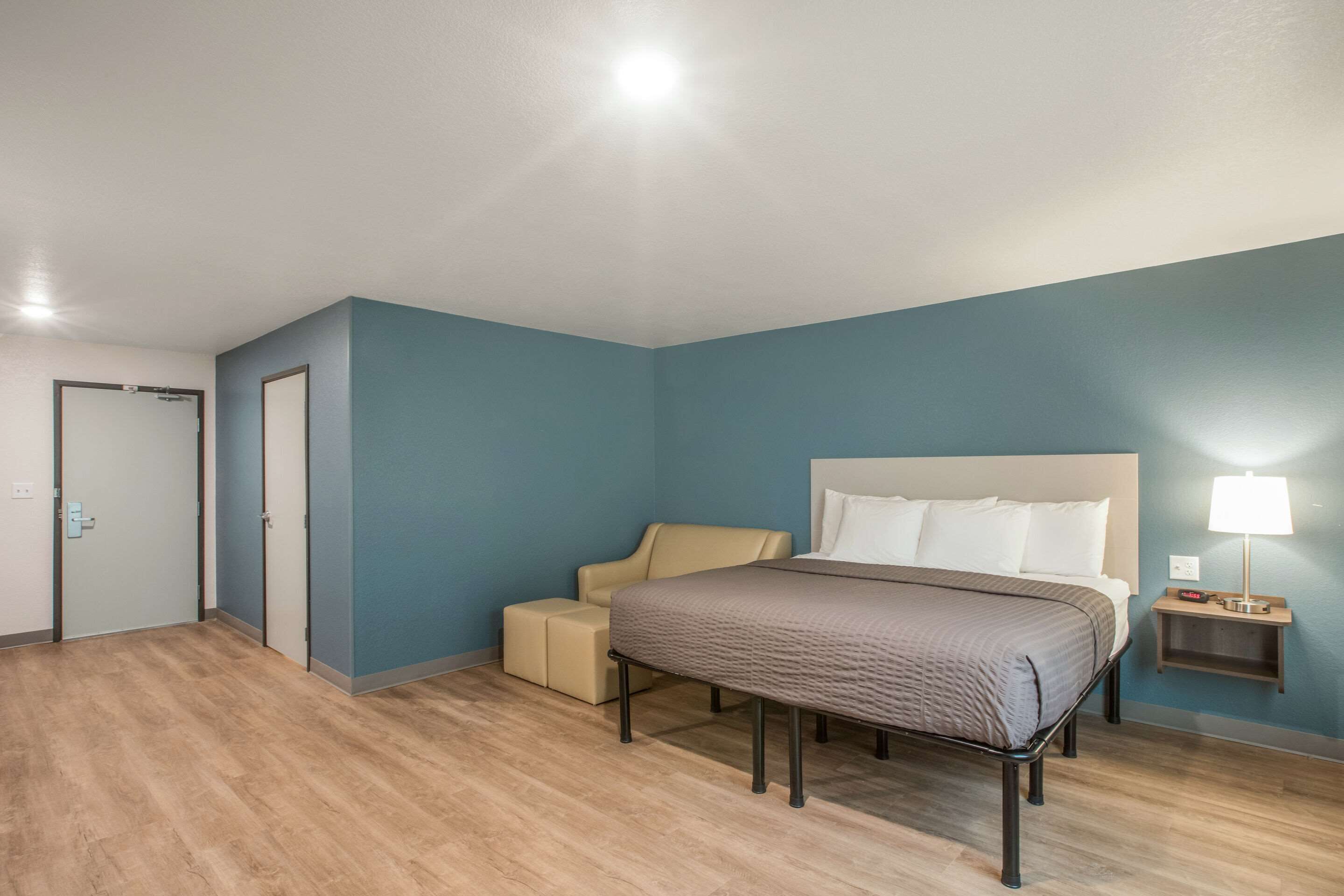 Une chambre d’hôtel avec un lit, une table de chevet avec une lampe, une chaise et une porte.