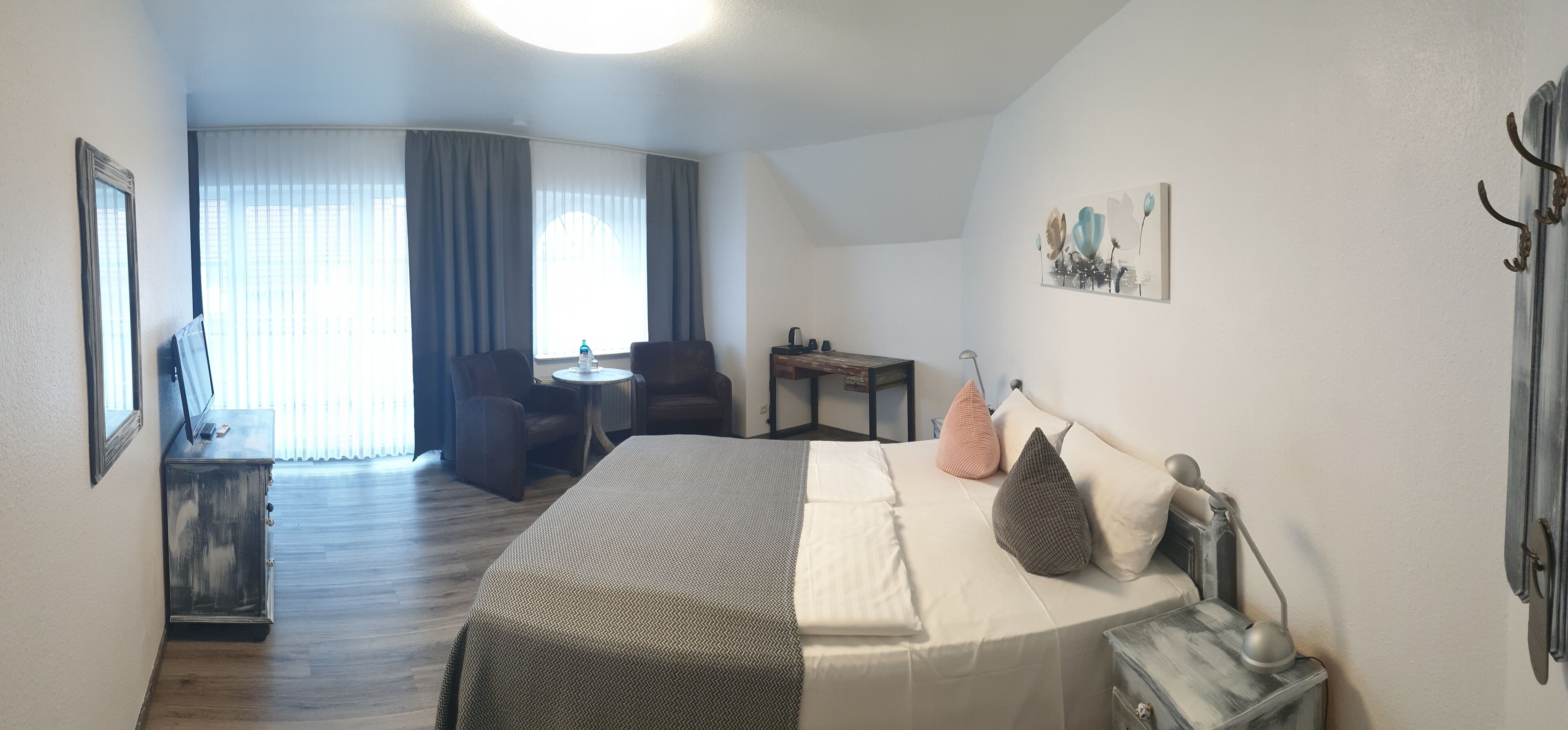 A hotel room with a bed, a desk, a chair, a small table, and a window with curtains.