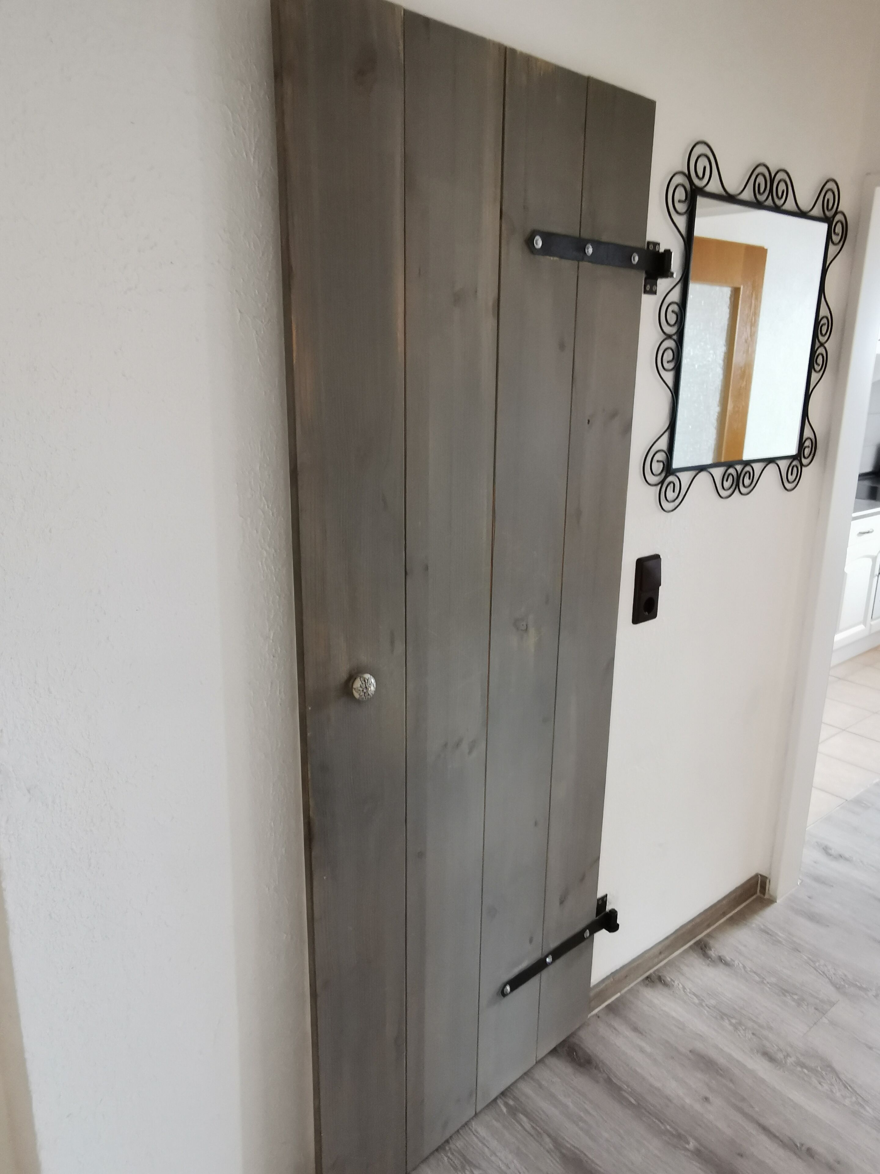 Una porta in legno con maniglia metallica e cornice nera in metallo, con uno specchio.