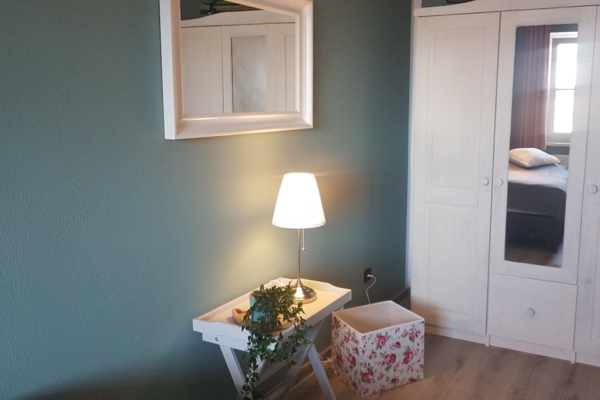 A bedroom with a bed, a bedside table with a lamp, a small plant, and a wardrobe.