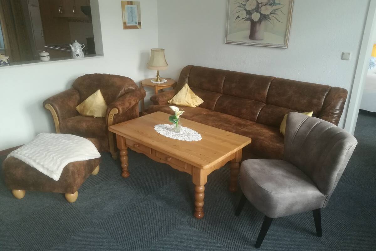 A living room with a brown sofa, a wooden coffee table, a grey armchair, and a small side table with a lamp.