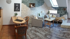 A cozy living room with a stone wall, a wooden dining table, a sofa, and a coffee table. - Ferienwohnungen Blischke (Wittmund)