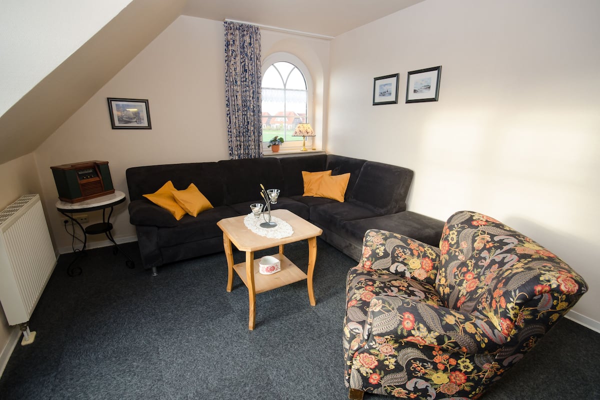 A cozy living room with a black sofa, a wooden side table, and a floral armchair.