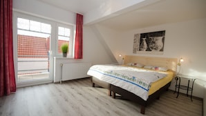 A bedroom with a bed, a window with curtains, a radiator, a potted plant, and a wall with a painting. - Ferienwohnungen Blischke (Wittmund)