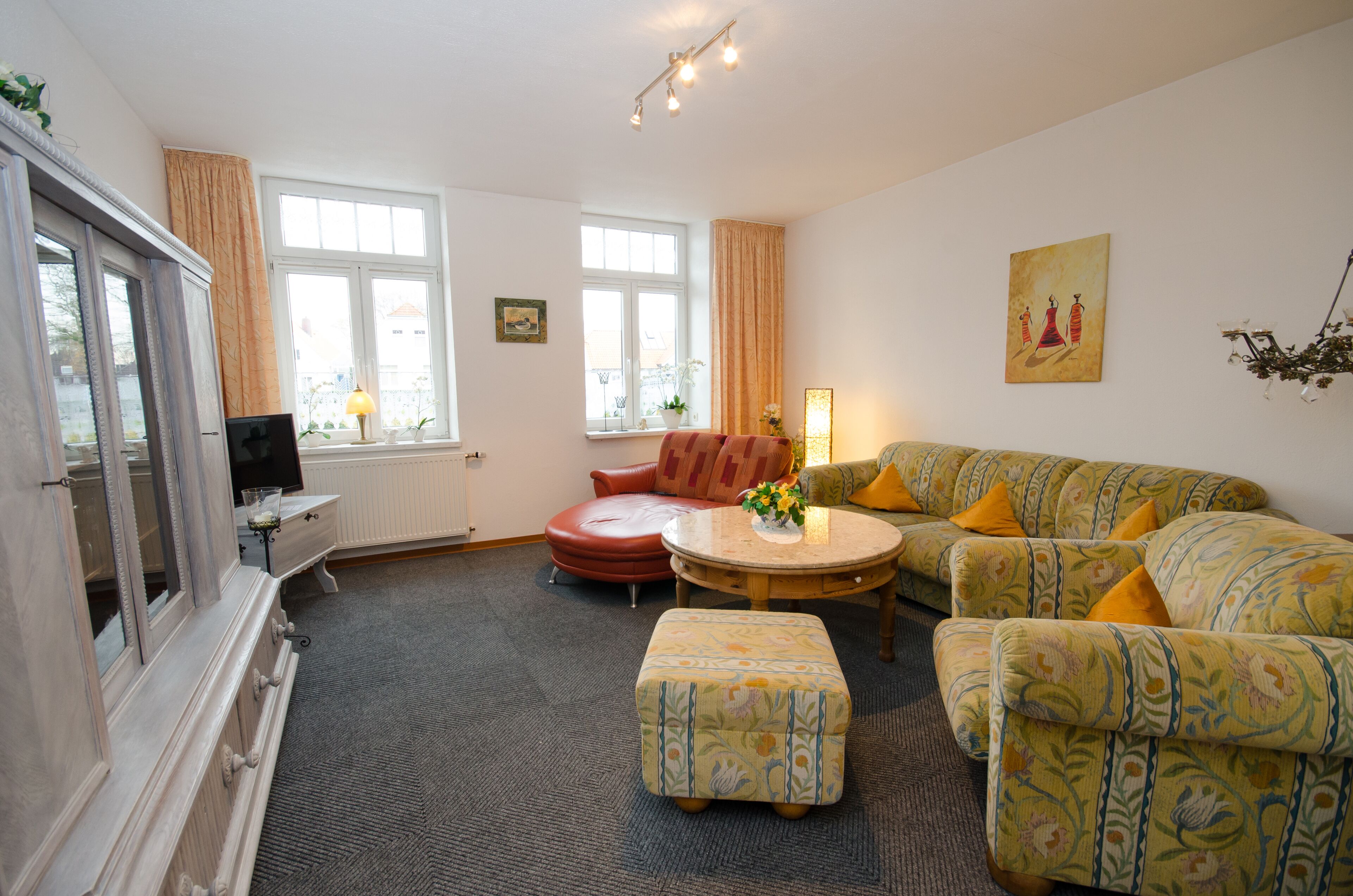 A living room with a sofa set, a red armchair, a small table with a vase, and a television on a cabinet.