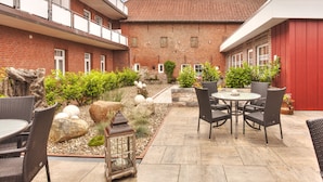 A courtyard with a brick building, outdoor seating, and potted plants. - Ferienwohnungen Blischke (Wittmund)