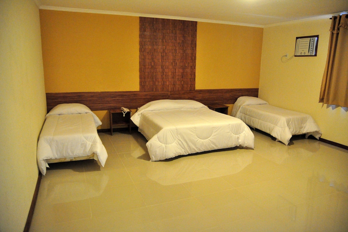 A hotel room with three single beds, a wooden headboard, and a wall-mounted telephone.