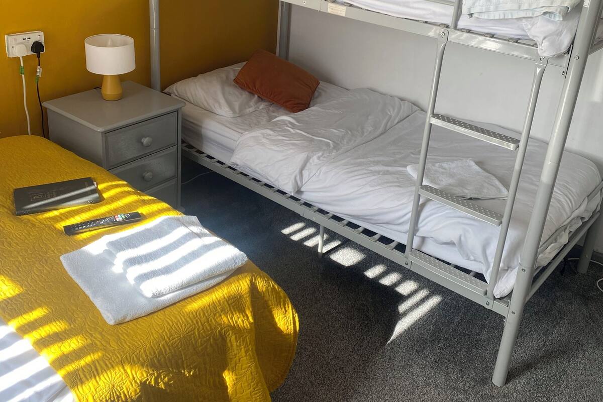 Ein Schlafzimmer mit Etagenbett, einer gelben Bettdecke, einem Nachttisch mit Lampe und einer Steckdose.