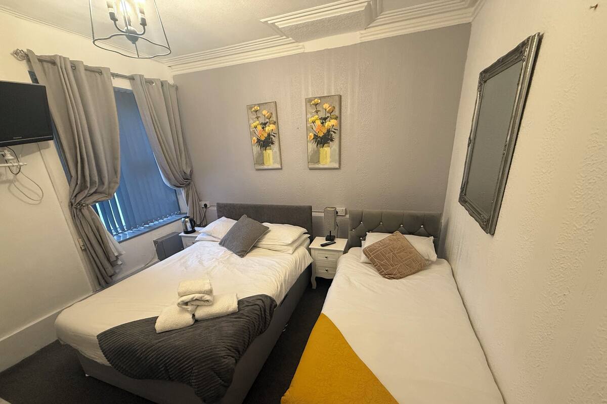 Ein Hotelzimmer mit zwei Betten, einem Fernseher, einem Fenster mit Vorhängen und zwei Bildern an der Wand.